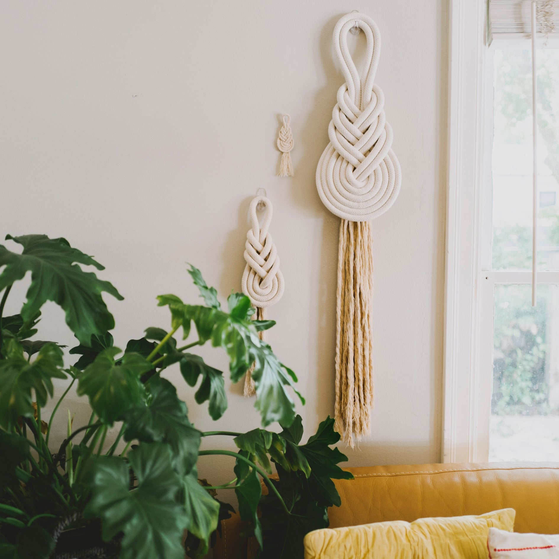 Macrame wall hanging with tassels on a light-colored wall with plants and a yellow couch