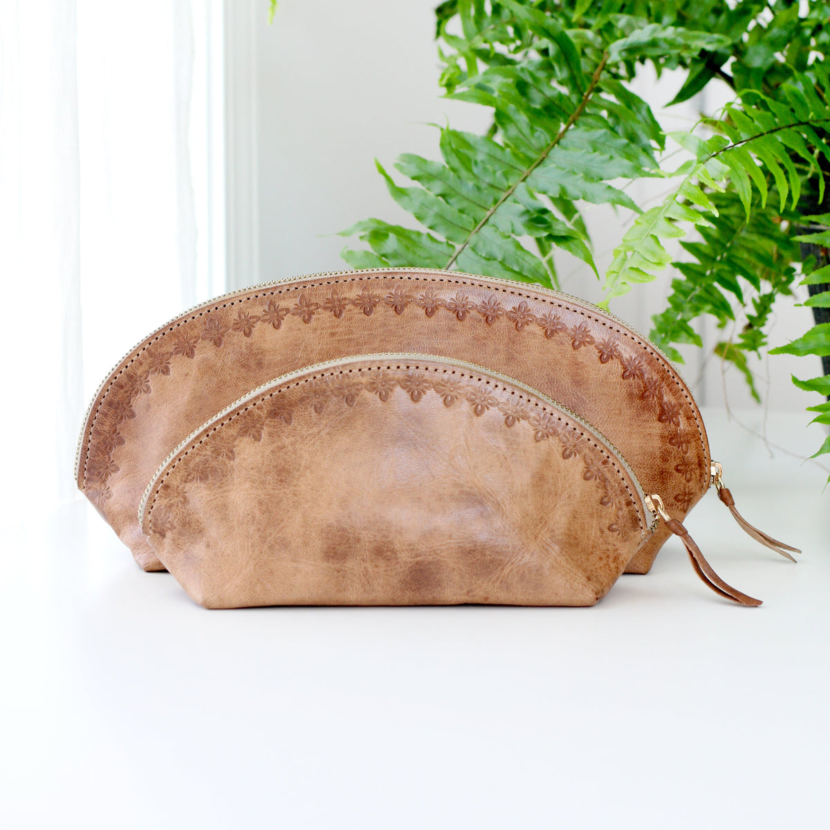 Two brown leather pouches on a white surface with green plants in the background