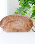 Two brown leather pouches on a white surface with green plants in the background