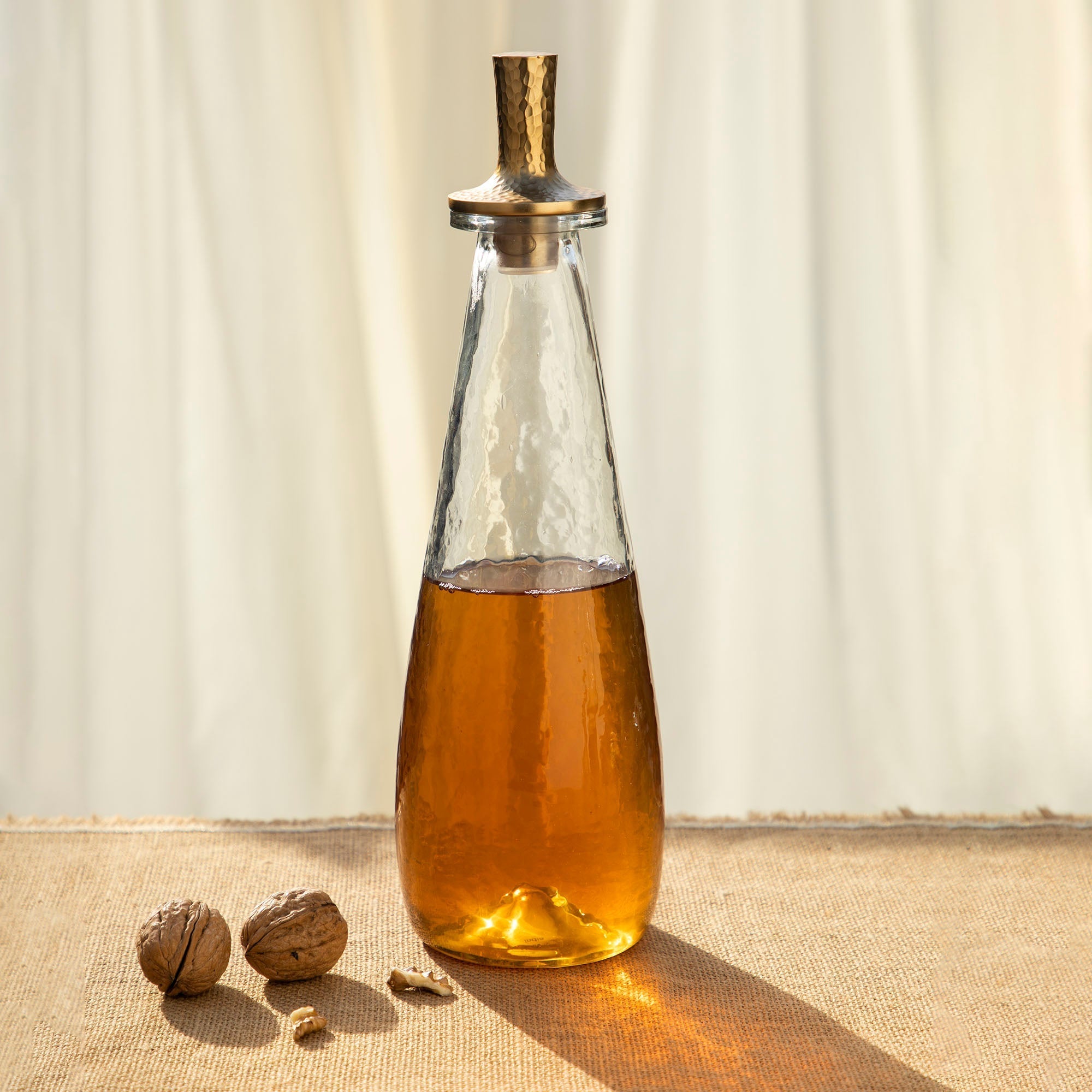 Glass decanter with a metal cap containing a amber liquid on a textured surface.