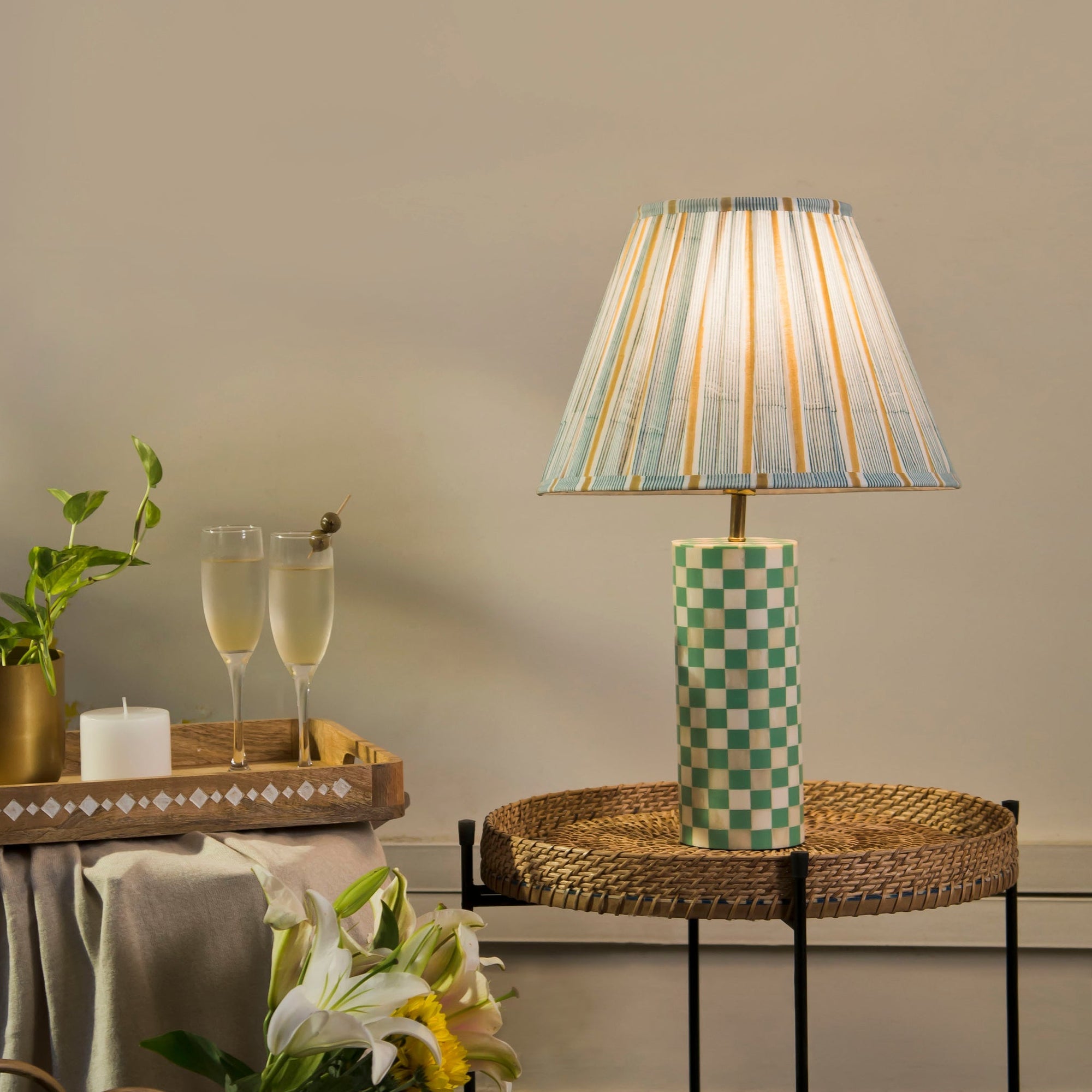 Decorative lamp with a checkered base on a table, accompanied by glasses of champagne and a plant.