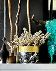 Decorative setup with a black and gold vase, white flowers, and a turquoise mosaic elephant against a dark background.