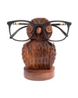 A hand-carved wooden owl eyeglass holder stand with a pair of glasses placed on it.