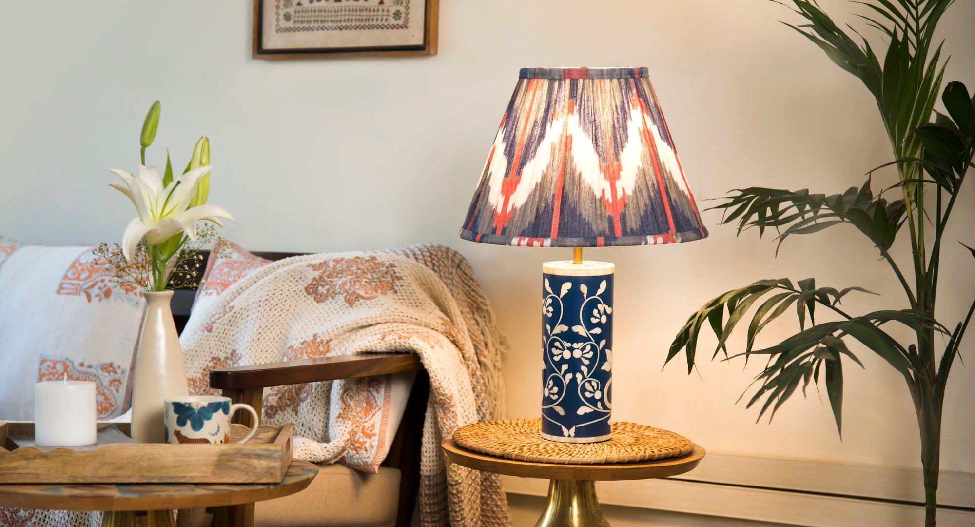 Decorative lamp with colorful shade on a table next to a chair with floral cushions and a plant.