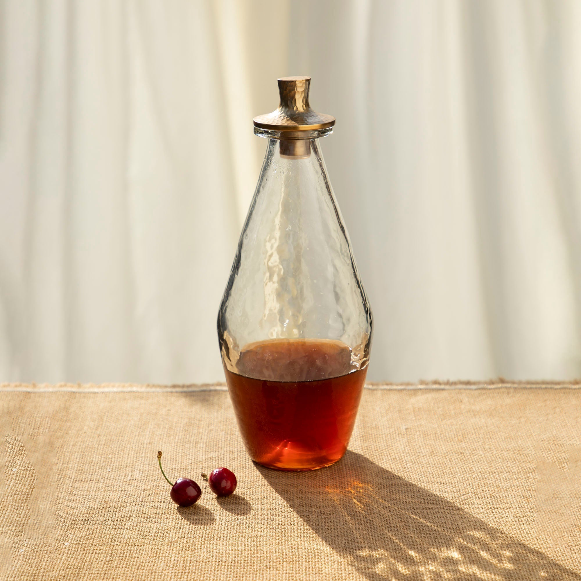 Glass decanter with a gold lid on a textured surface with cherries nearby