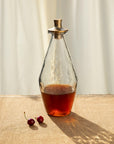 Glass decanter with a gold lid on a textured surface with cherries nearby