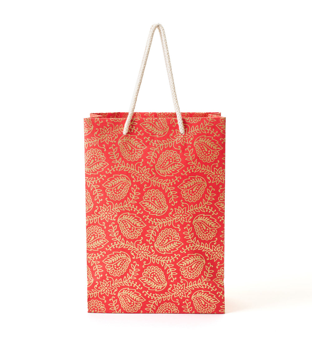 Red paper bag with gold paisley pattern and rope handle on a white background