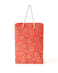 Red paper bag with gold paisley pattern and rope handle on a white background