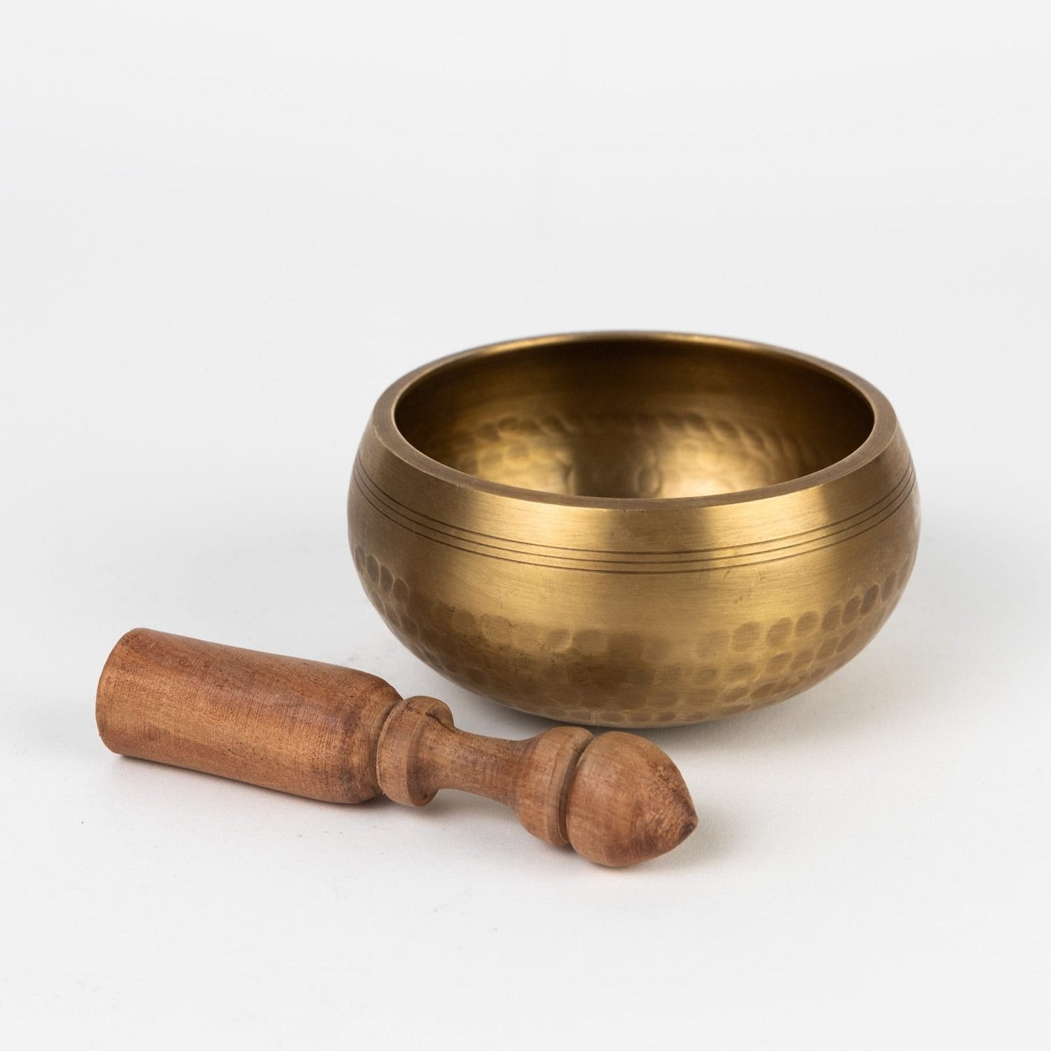 Bronze singing bowl with wooden striker on a white background