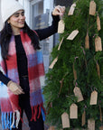 Woman decorating a Christmas tree with gift tags outdoors.