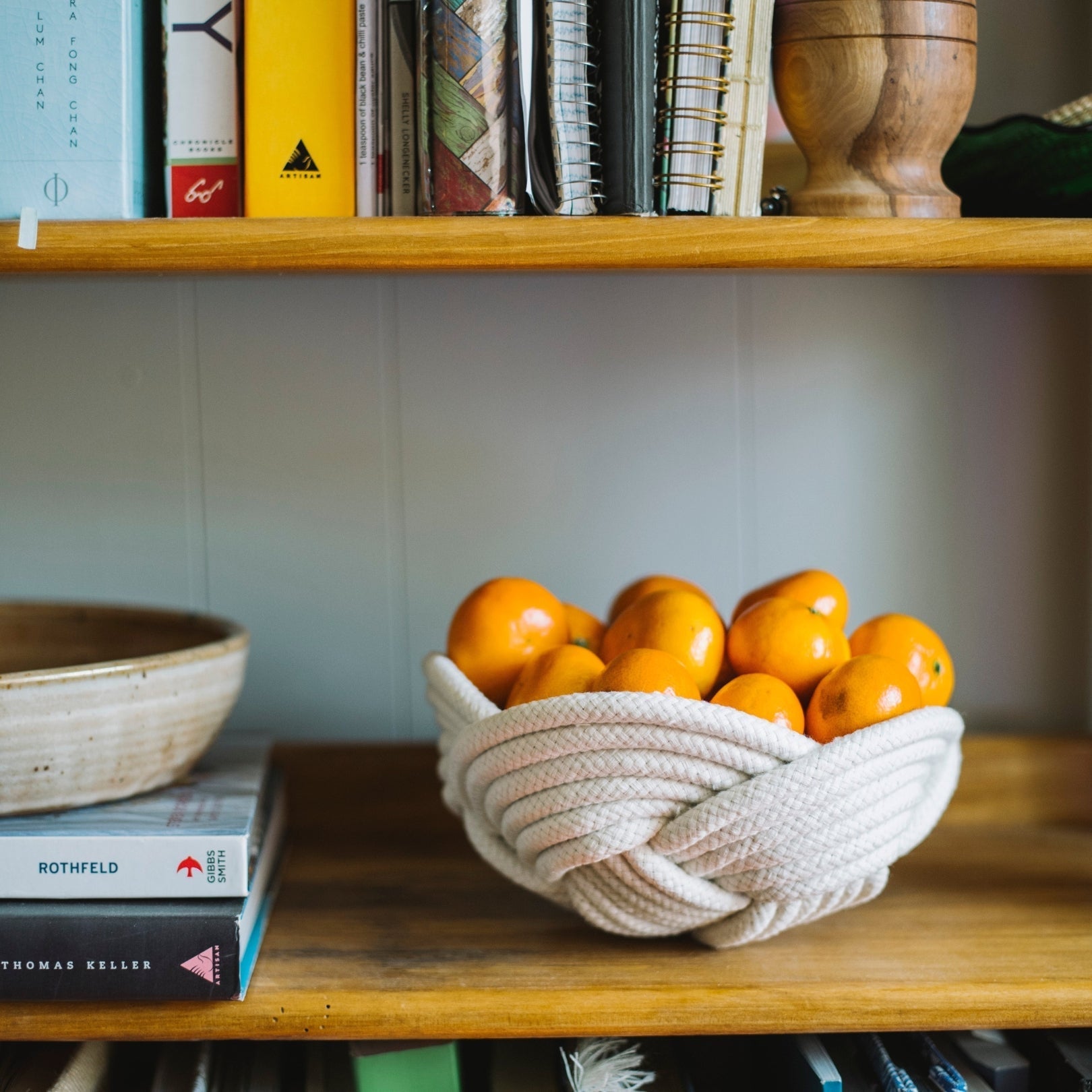 Bowl of oranges on a wooden shelf with books and a woven basket