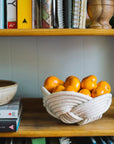 Bowl of oranges on a wooden shelf with books and a woven basket