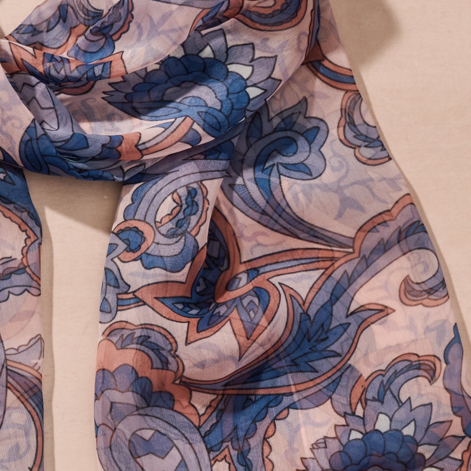 Close-up of a patterned fabric scarf with blue and orange designs on a beige background