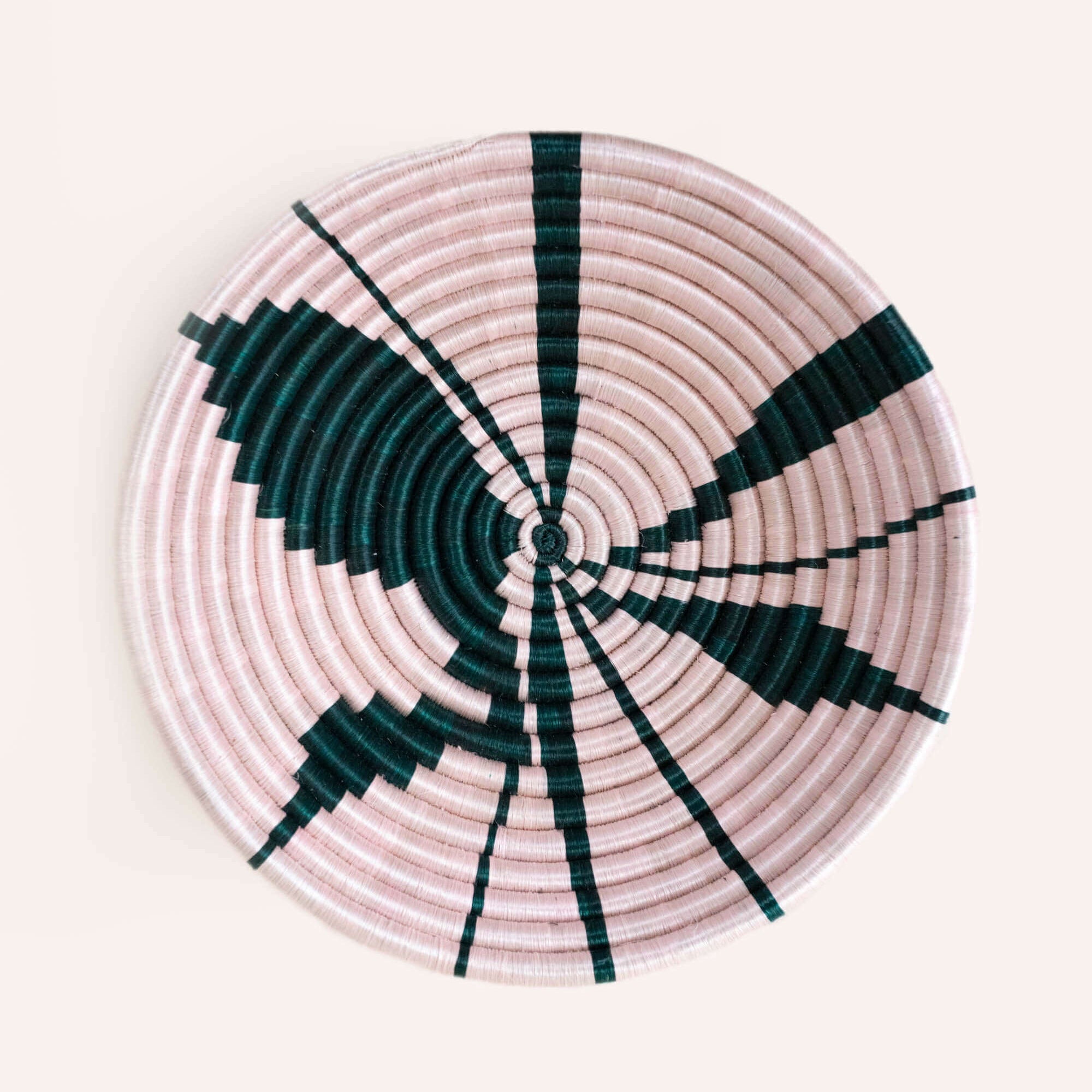 Round woven basket with pink and green pattern on a white background