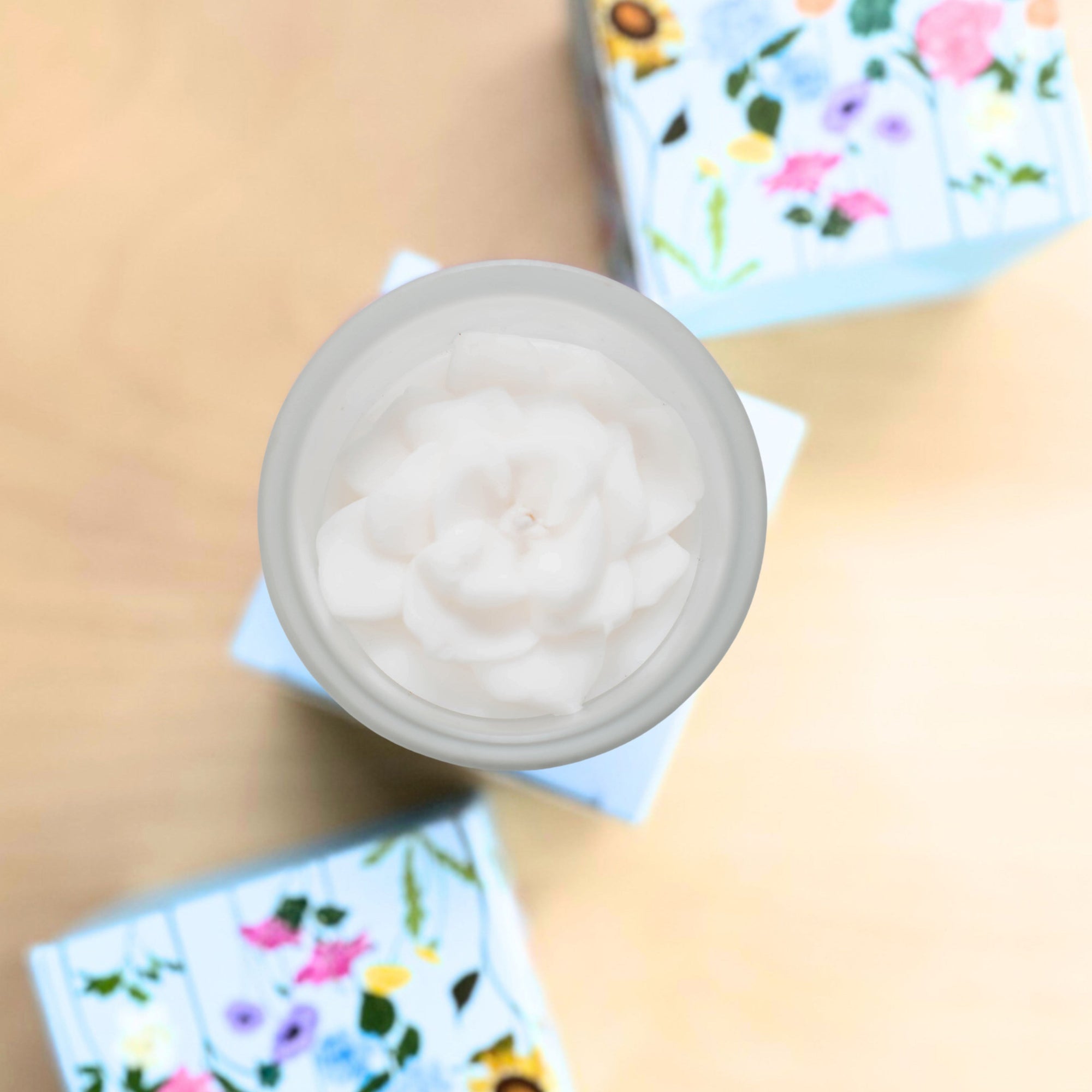 Top view of a container with a white flower candle on a beige surface with floral designs.