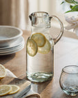 Clear glass pitcher with lemon slices on a wooden table with white flowers in the background