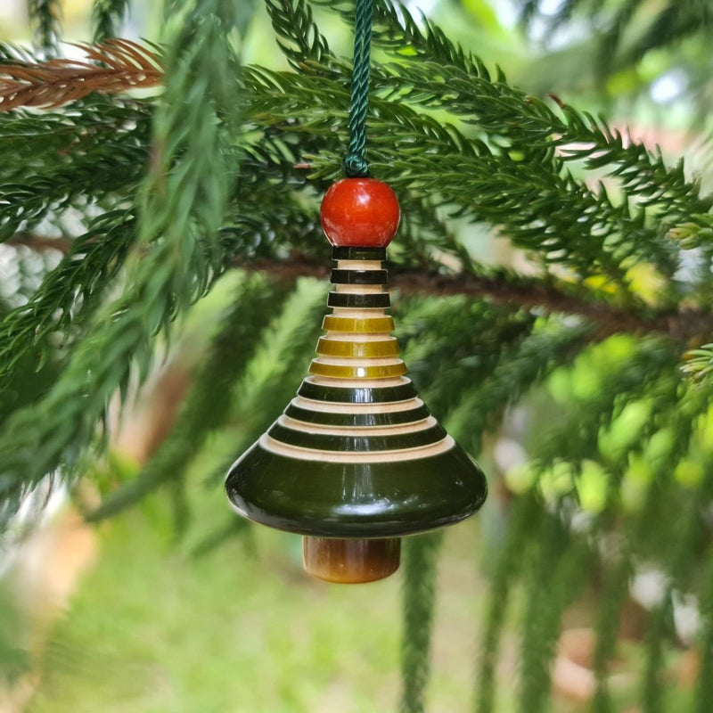 Decorative hanging ornament with a bell and striped design and red top on a christmas tree branch.