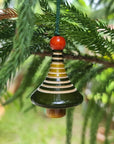 Decorative hanging ornament with a bell and striped design and red top on a christmas tree branch.