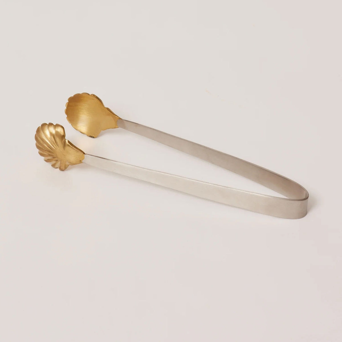 Gold and silver tongs on a light beige background