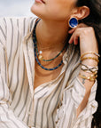 Woman wearing layered necklaces, earrings, and bracelets with a blurred background