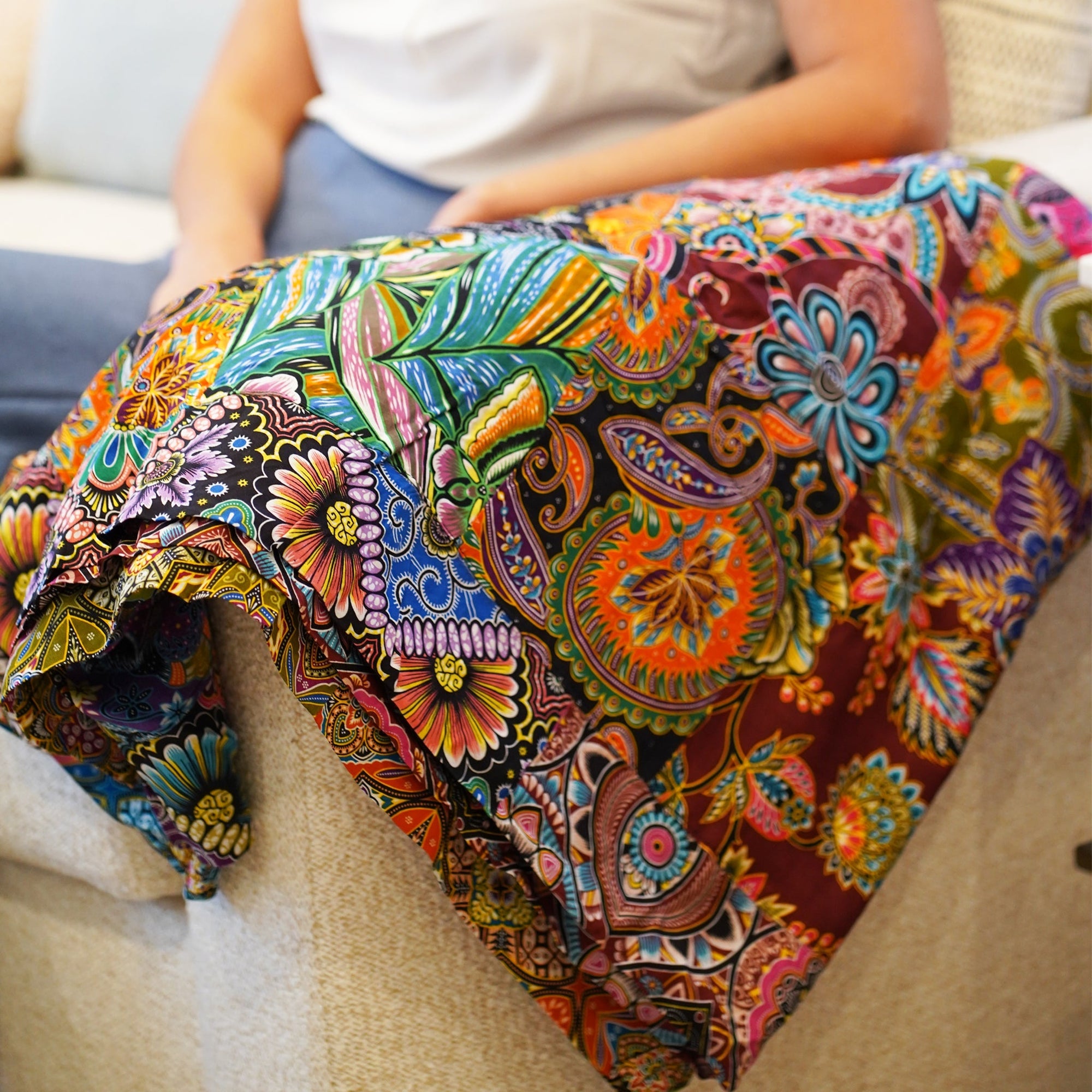 Colorful patterned quilt draped over a person sitting on a couch.
