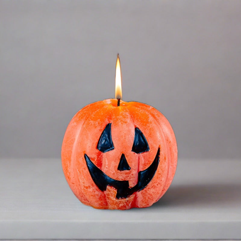 Pumpkin-shaped candle with a jack-o'-lantern face on a gray background