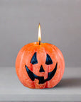 Pumpkin-shaped candle with a jack-o'-lantern face on a gray background