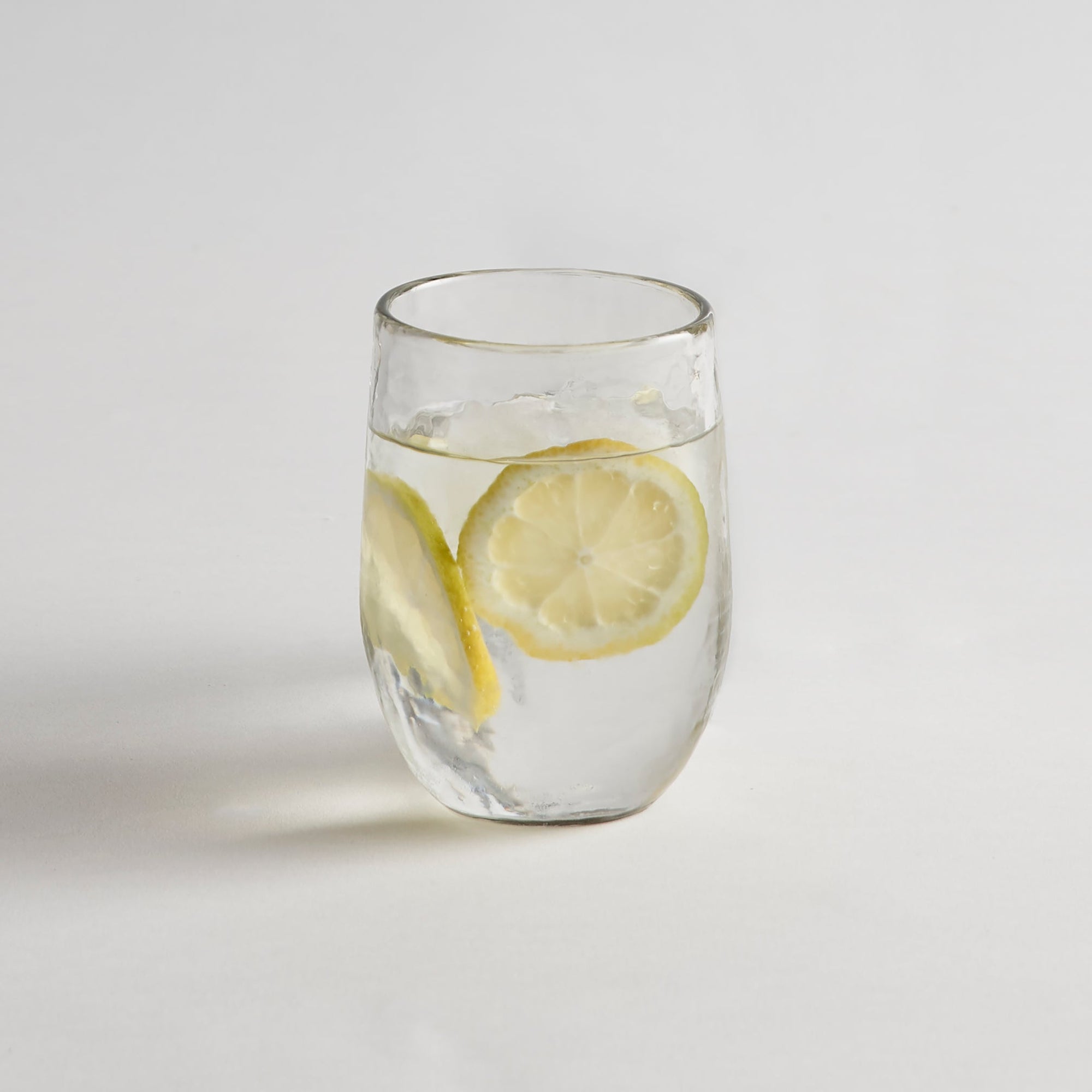 A clear glass with water and lemon slices on a white background, resembling one of the glasses in the set.