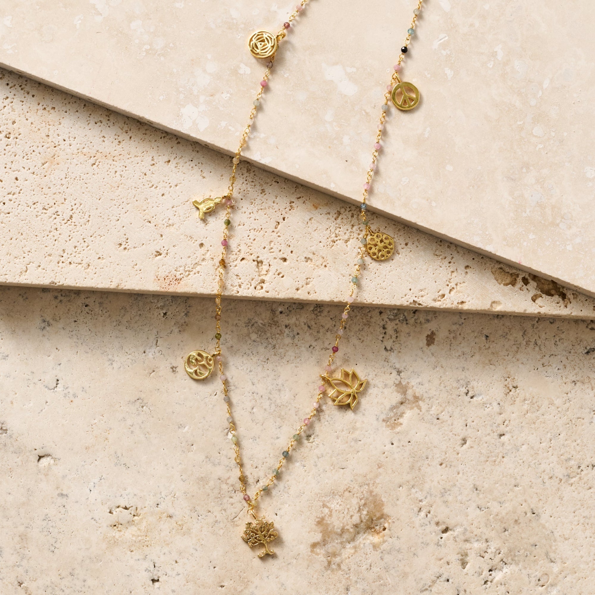 Gold necklaces with floral pendants on a textured beige surface