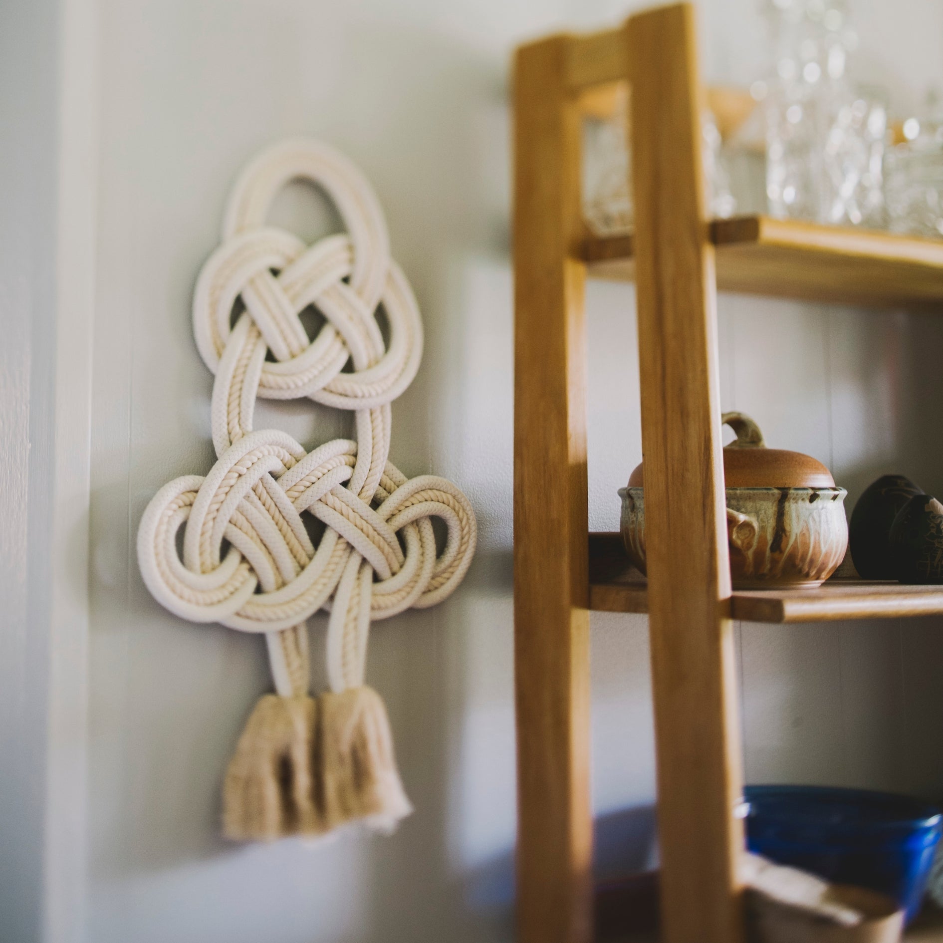 Decorative cotton wall piece with braided design on a wall next to a wooden shelf.