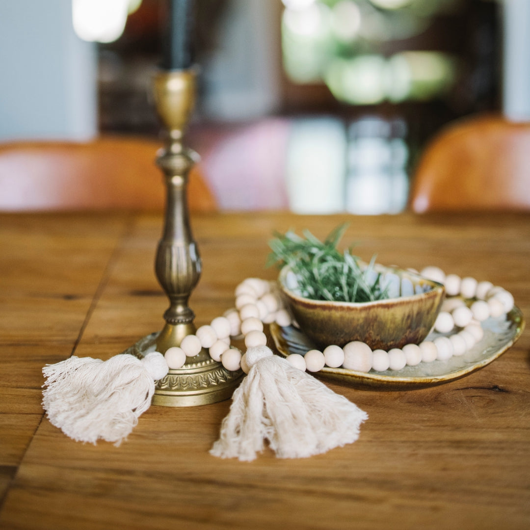 Decorative items on a wooden table including a brass candlestick, beads, and a small bowl with greenery