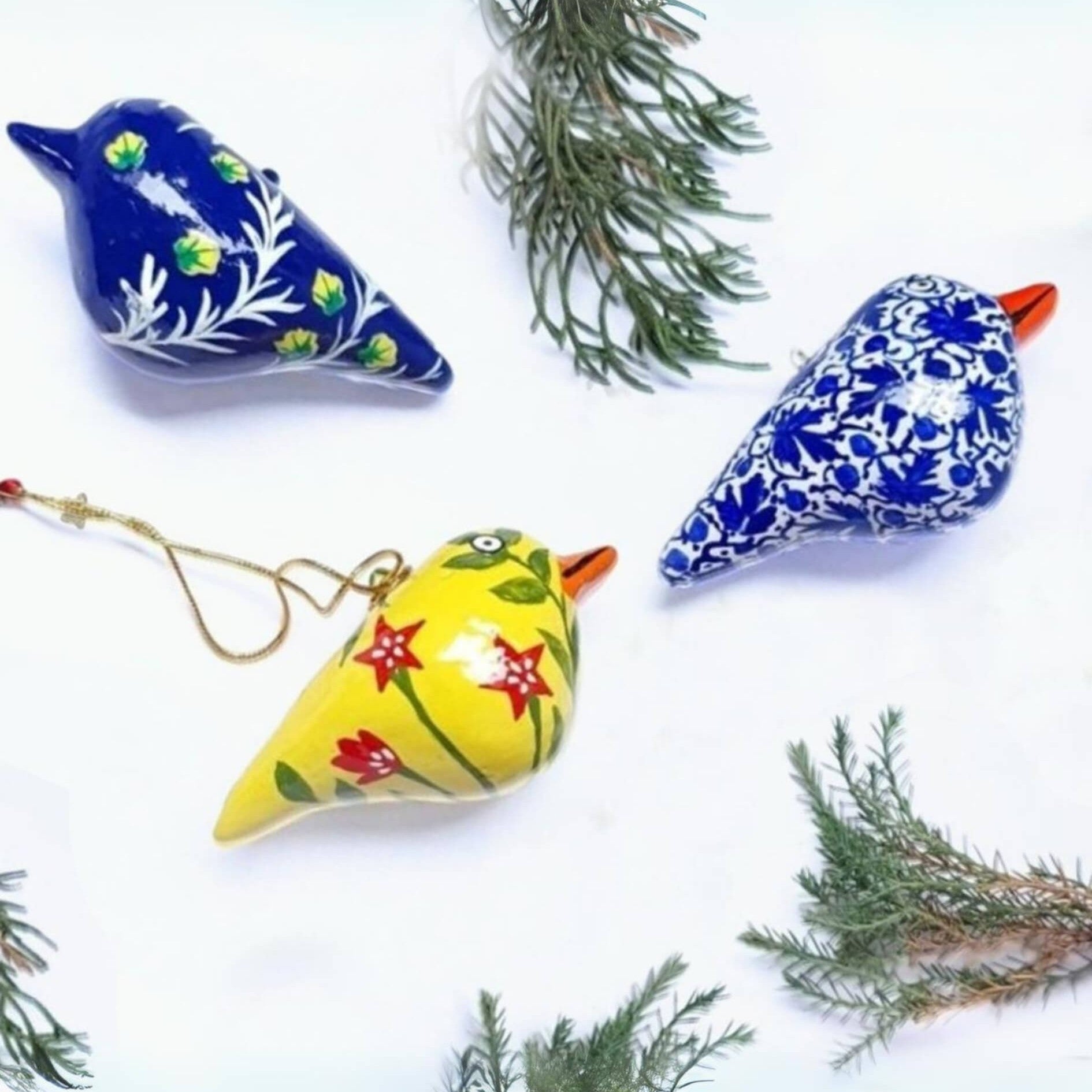 Decorative papier-mâché bird ornaments with floral patterns on a white background with greenery