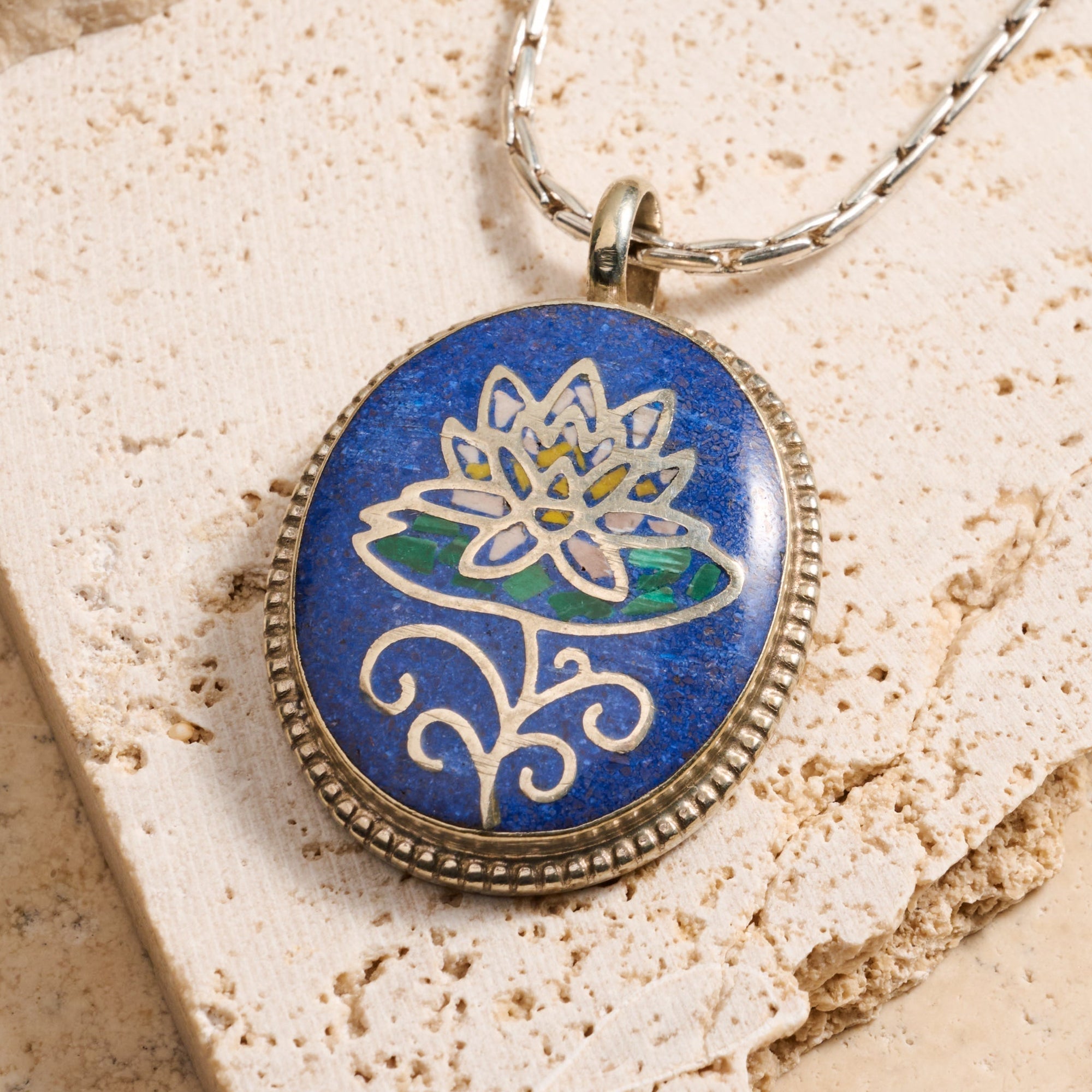 Necklace with a pendant featuring a lotus flower design on a textured stone surface