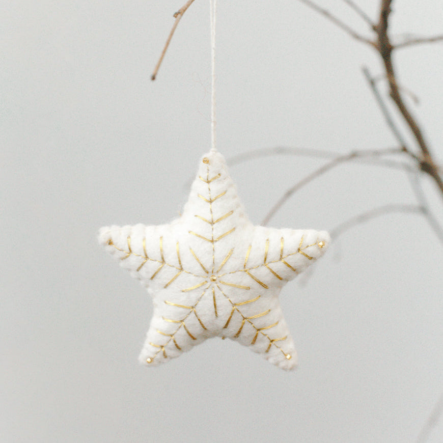 Star-shaped decorative ornament with gold embroidery on a branch against a light background