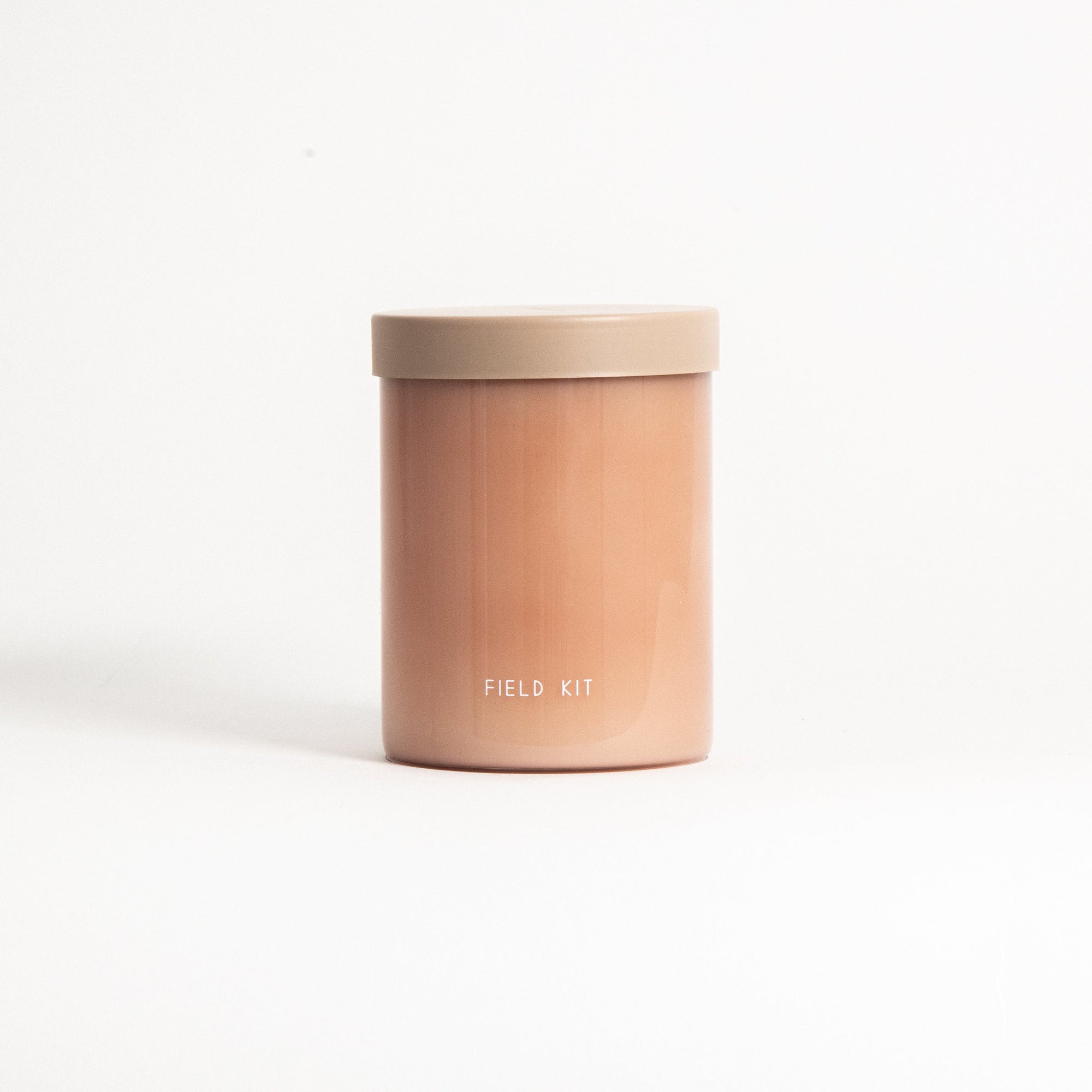 A pink cylindrical candle with the brand 'Field Kit' visible on the label, housed in a reusable glass jar